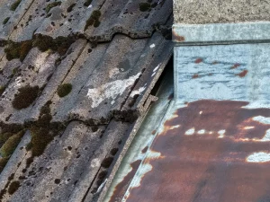 Nahaufnahme eines beschädigten Dachziegels neben einer stark verrosteten Blechabdeckung, aufgenommen bei einer Drohneninspektion.